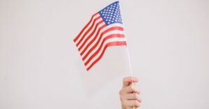A hand holding up a small American flag against a plain light background