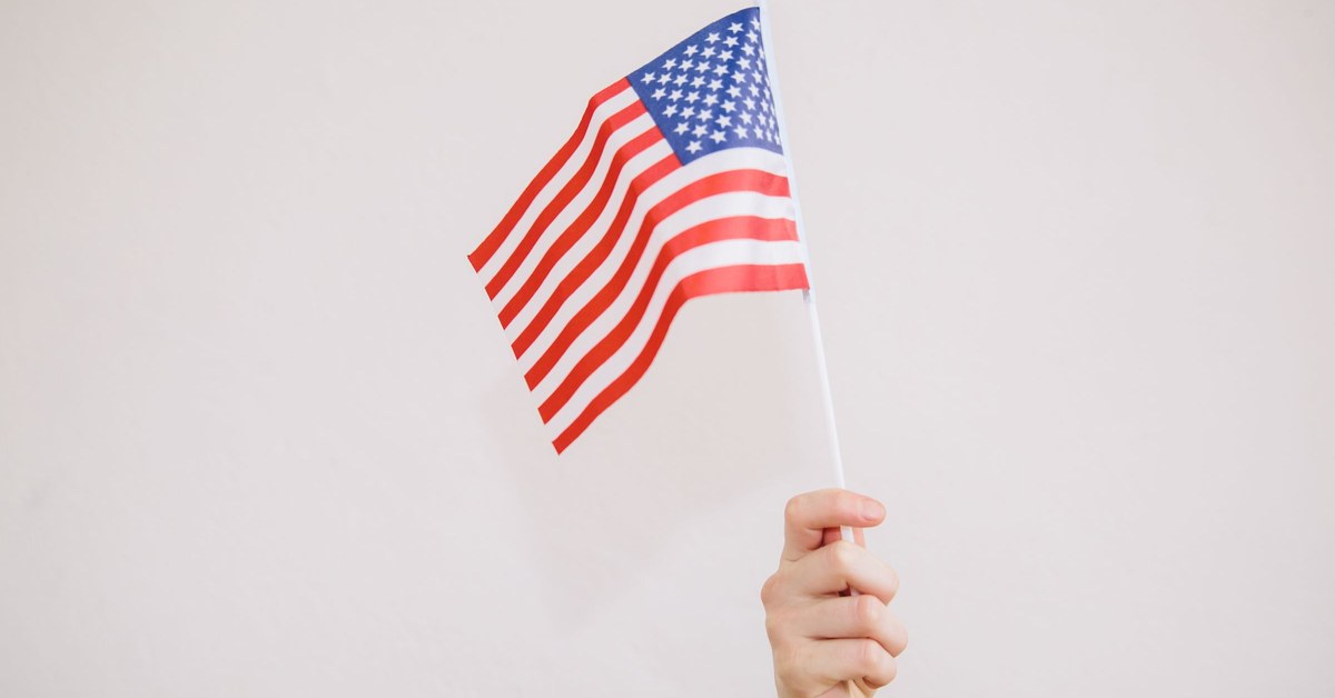 A hand holding up a small American flag against a plain light background